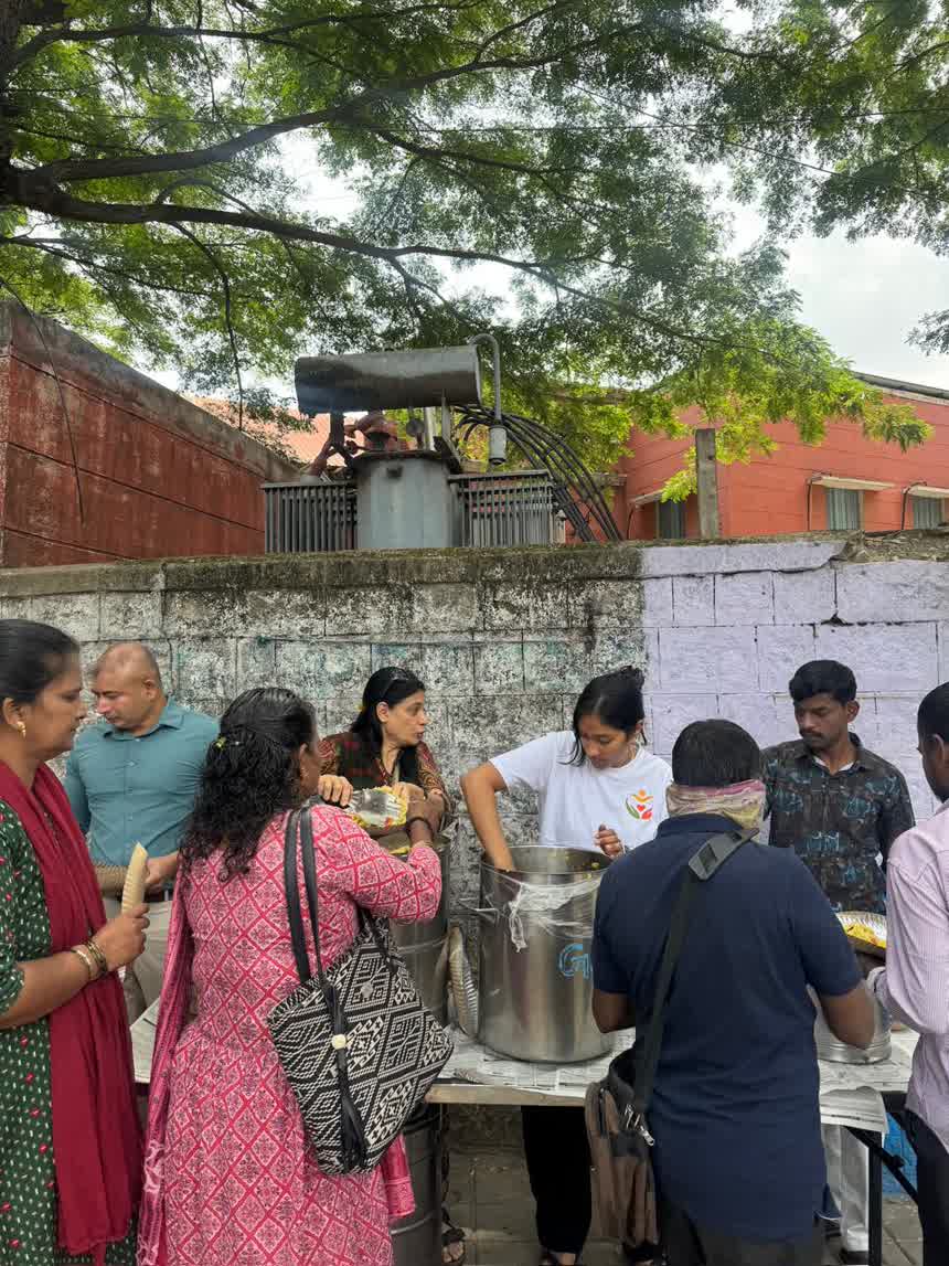 Volunteers serving food from large steel vessels onto paper plates at a roadside table