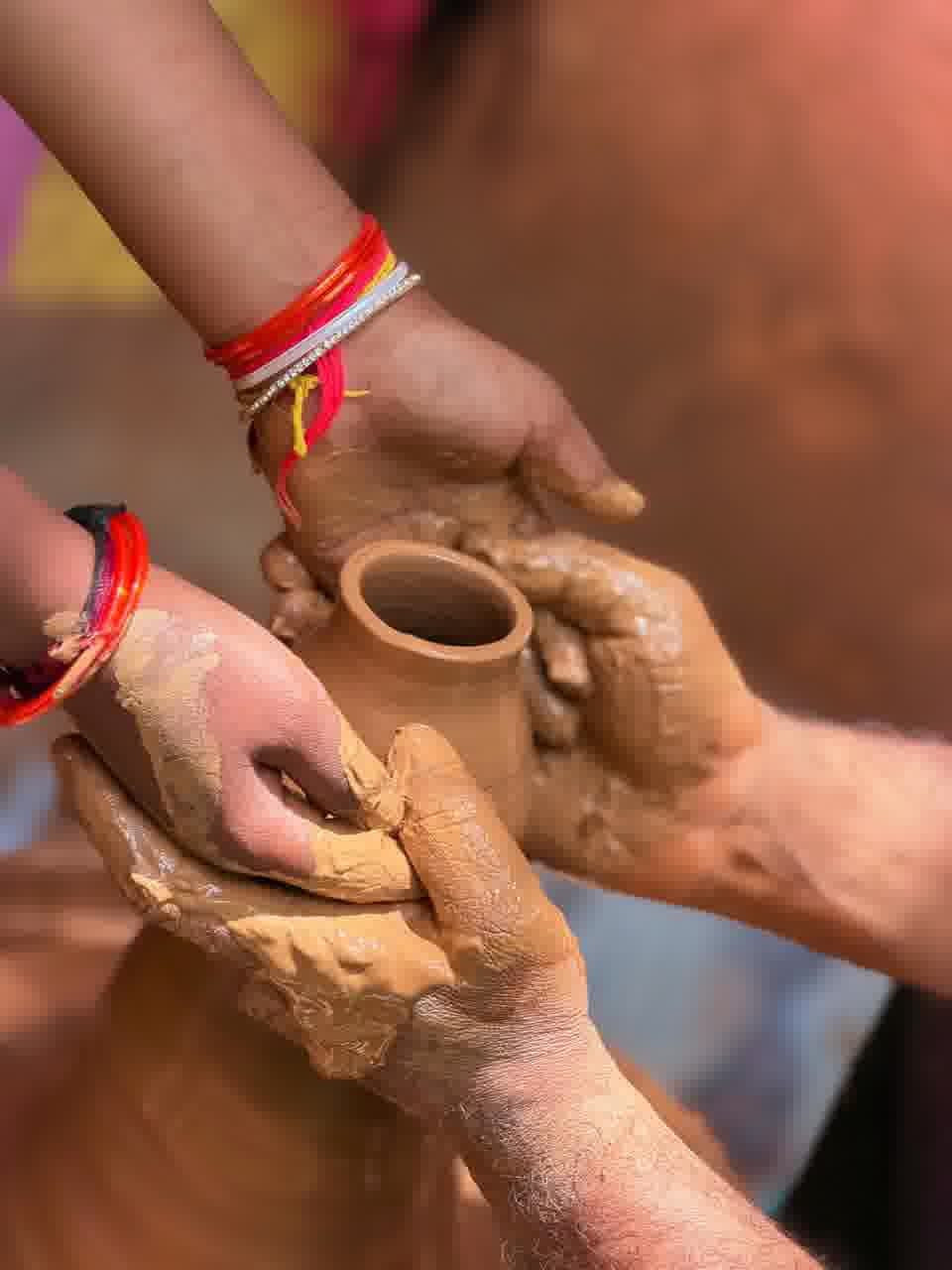 Close-up of a child's hands and a volunteer's hands shaping a wet clay pot on the pottery wheel
