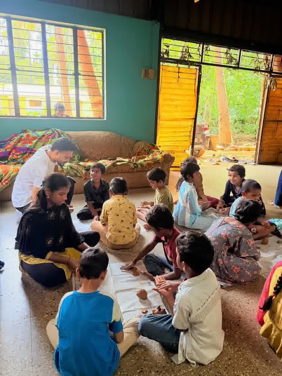 Children sitting in a circle on the floor shaping clay, with volunteers among them