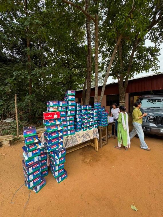 Boxes of new footwear stacked under the trees at the gurukul, with volunteers setting up the table